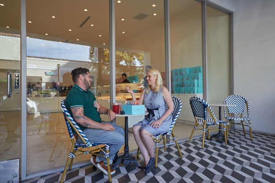 A couple chatting at an outdoor café table in front of a bakery