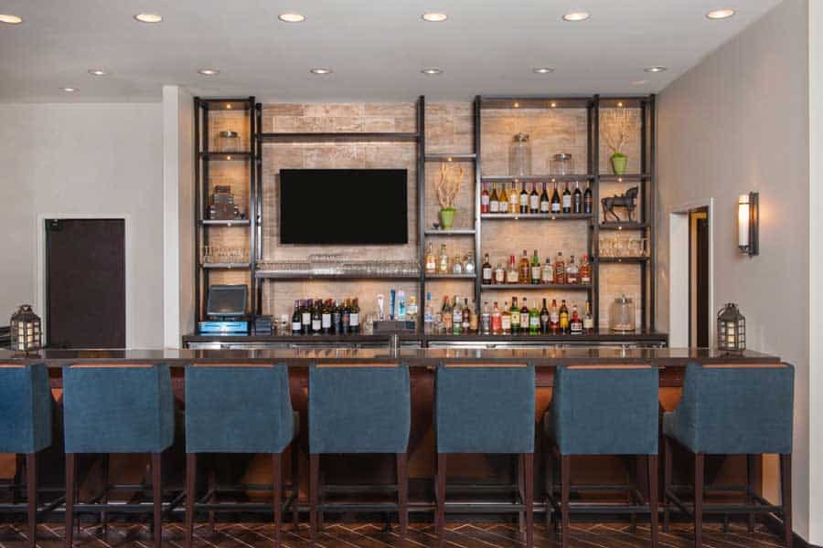 A modern hotel bar with blue barstools and shelves of wine and liquor