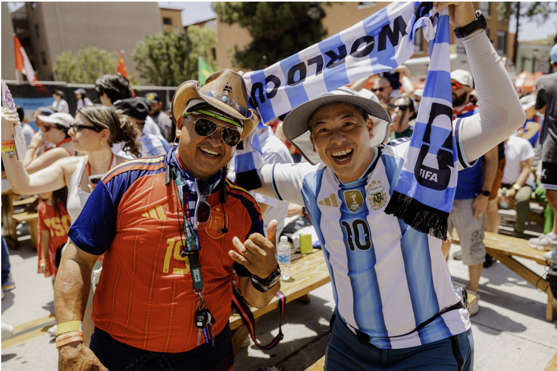 Two smiling soccer fans in Spain and Argentina jerseys hold up a World Cup scarf at the Fan Zone