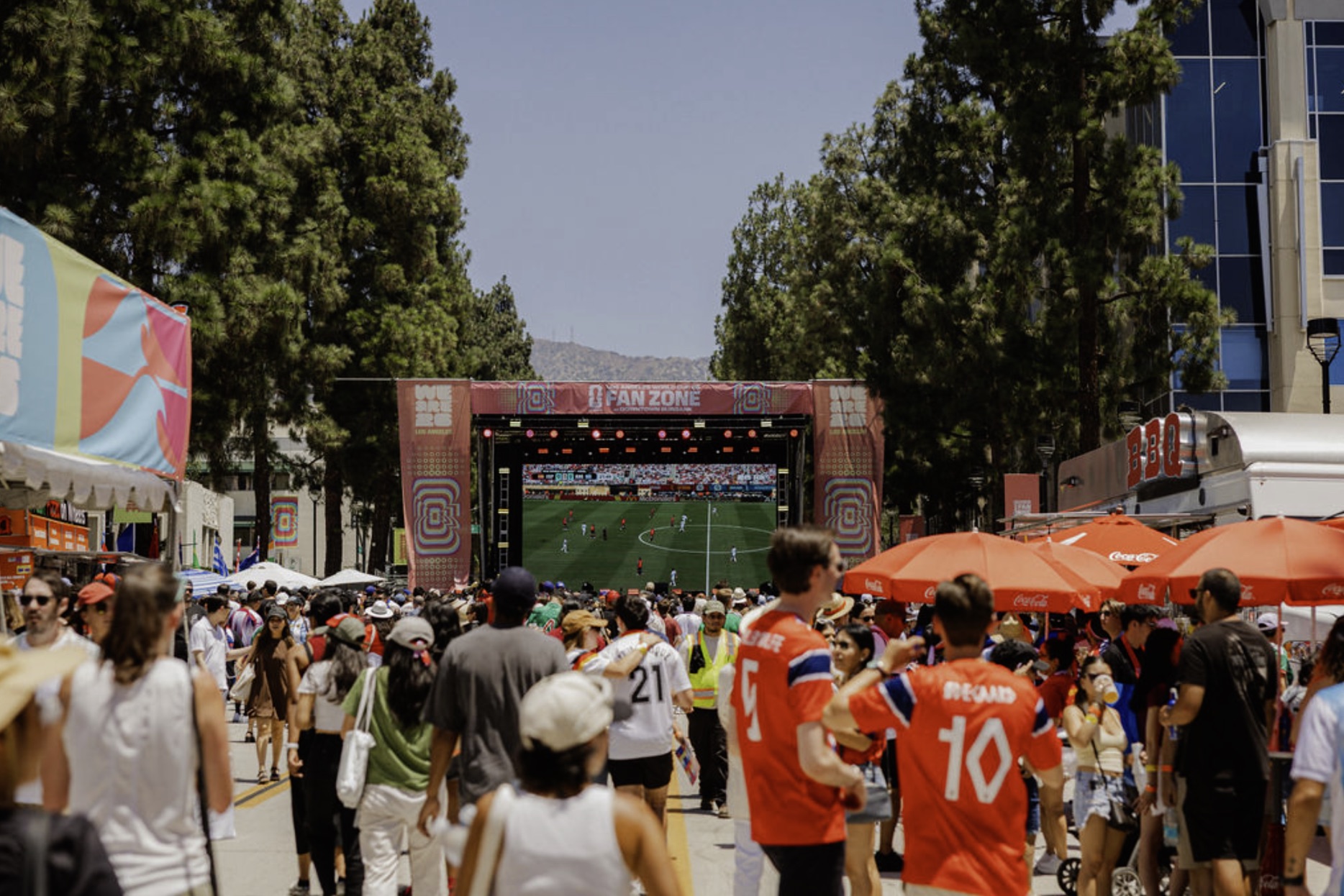 Soccer fans walk toward the Los Angeles World Cup 26 Fan Zone screen on a sunny day in Downtown Burbank